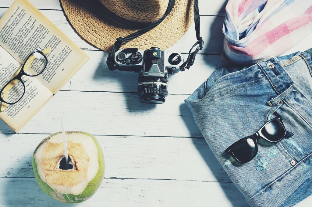 Open travel suitcase with casual jeans, stylish sunglasses, and a tropical coconut packed together, representing a vacation package ready for adventure.