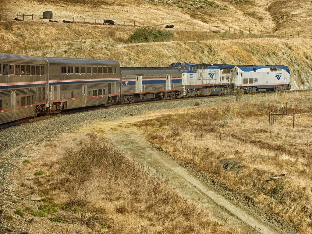 Amtrak train traveling through scenic countryside in the USA, showcasing classic American rail travel with bright blue passenger cars and clear skies.